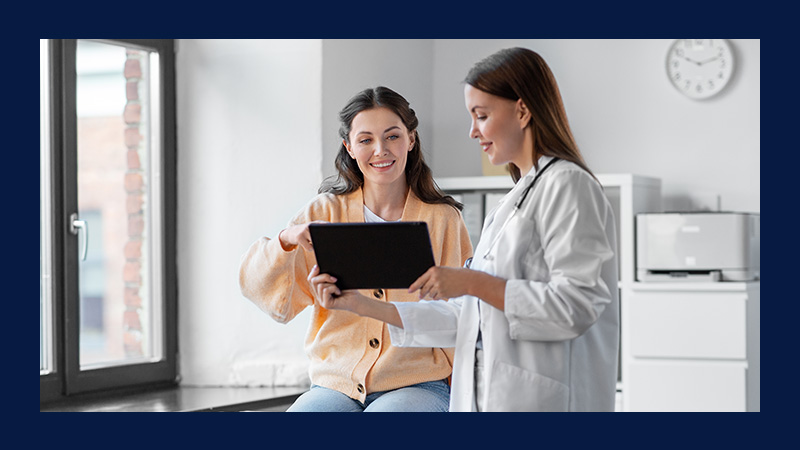 A doctor and patient smiling while looking at a tablet in a bright, modern office, conveying a sense of trust and positive communication.